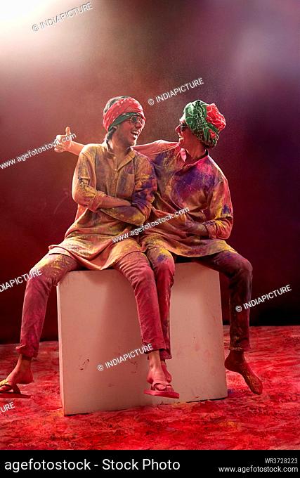 TWO YOUNG MEN WEARING PAGDI AND GOGGLES ENJOYING HOLI FESTIVAL TOGETHER