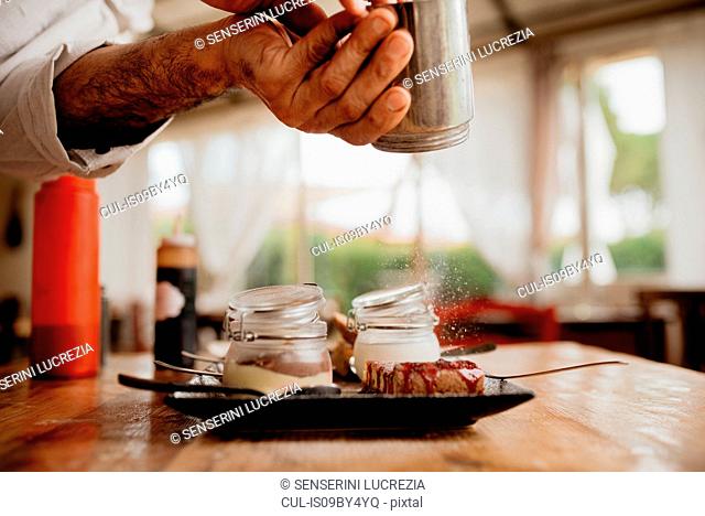 Chef sprinkling icing sugar on dessert