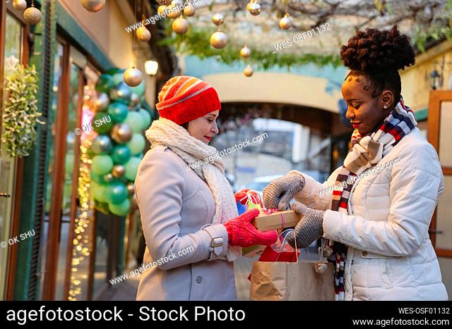 Woman in warm clothing giving gift to friend on Christmas festival