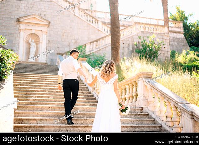 The bride and groom climb the ancient stairs of the Nativity of the Blessed Virgin Mary church in Prcanj. High quality photo