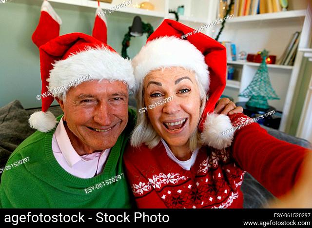 Portrait of senior couple in santa hat sitting on couch and smiling looking at camera at home