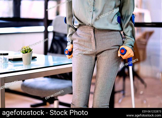 Handicapped Businesswoman Walking With Crutches At Workplace
