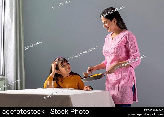A HAPPY DAUGHTER LOOKS AT MOTHER WHILE SHE SERVES FOOD