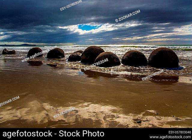 Moeraki boulders - group of large round boulders. The coast of New Zealand. The sun's rays are reflected in the ocean water