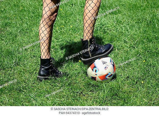 ILLUSTRATION - A young woman wearing fishnet stockings has placed her right foot on a football, on a green lawn, 21.05.2017