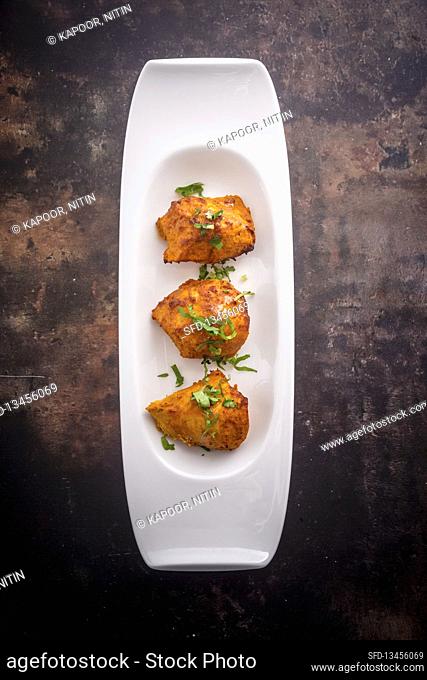 Chicken tikka (India) on a serving platter against a dark background