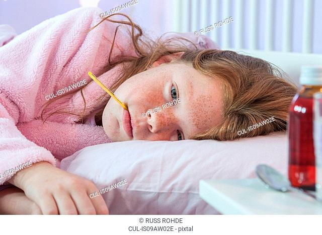 Close up of girl lying in bed with thermometer in her mouth