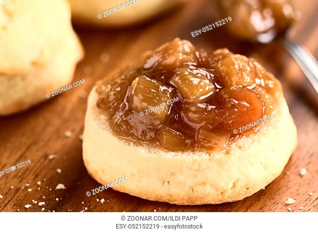 Homemade rhubarb jam on scone, photographed on wooden plate (Selective Focus, Focus one third into the jam)