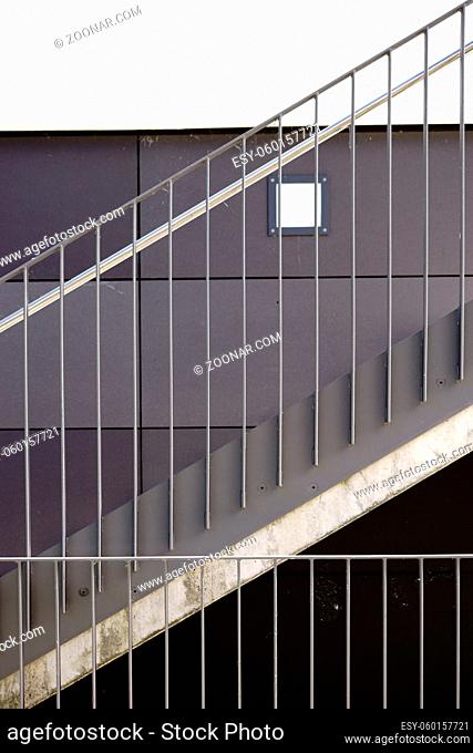 Das Detail einer modernen Treppe mit einem Geländer aus Edelstahl und einer Wandleuchte