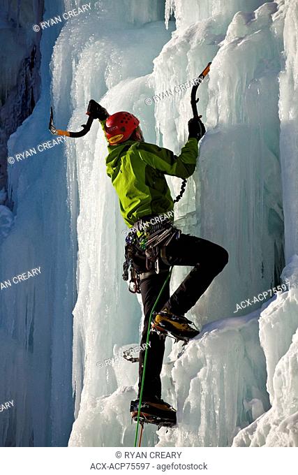 A male ice climber works his way the beautiful sunny ice climb called Malignant Mushroom WI5 in the Ghost River Valley, AB
