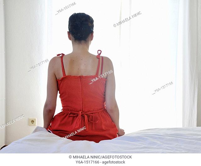 Young woman sitting on bed, rear view