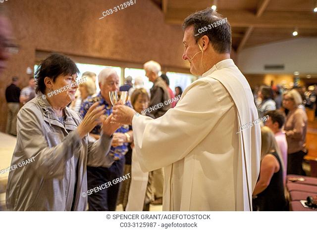 A robed deacon offers the communion cup to a senior woman parishioner at the conclusion of mass at a Catholic Church in Laguna Niguel, CA