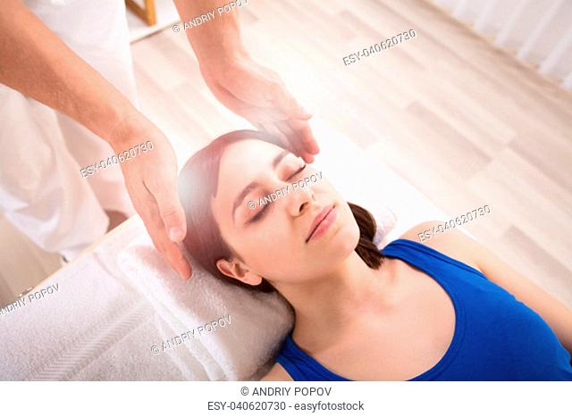 Close-up Of Therapist's Hand Performing Reiki Treatment On Young Woman In Spa
