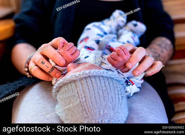 A selective focus abstract view of a mother and newborn infant at home. Baby boy grabs fingers of modern parent with tattooed arms