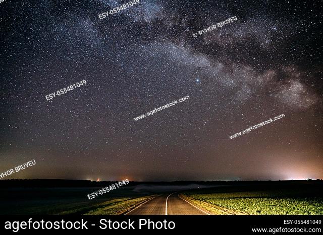 Blue Night Starry Sky Above Country Asphalt Road In Countryside And Green Field. Night View Of Natural Glowing Stars And Milky Way Galaxy