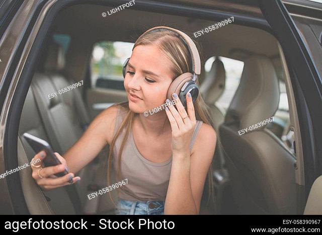 Cute teenage girl listening to her favorite music/audiobook on hig-end headphones during a roadtrip