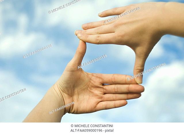 Hands making a finger frame in front of sky