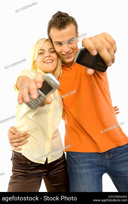 Happy young man and woman are showing mobile's screen to the camera. Isolated on white background in studio
