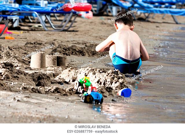 little boy in blue sea playing with mud pies and sand