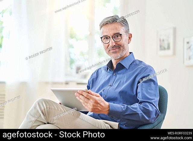 Smiling businessman holding tablet PC in armchair at home