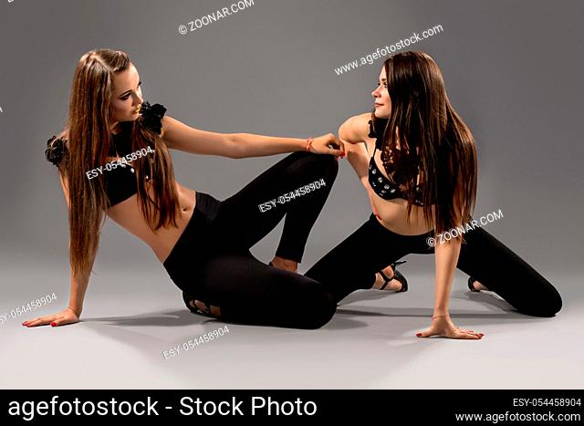 Two beautiful sexy dancers with fit bodies wearing erotic scenic clothes and high heels dancing at studio on grey background