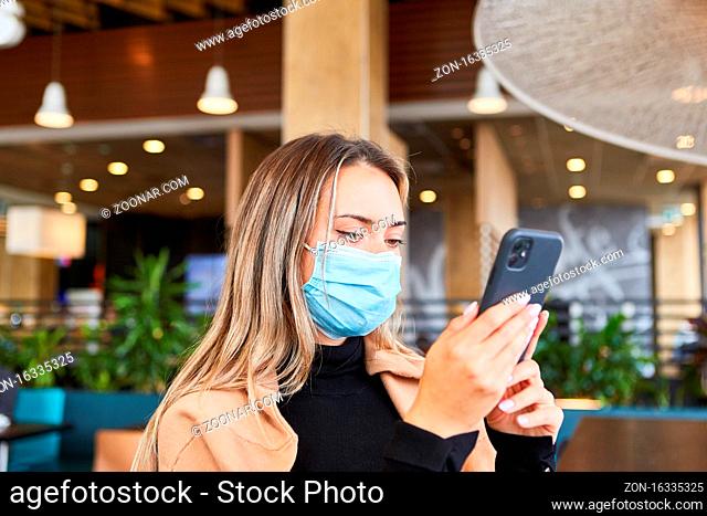 Junge Frau mit Mundschutz wegen Covid-19 liest SMS Warnung auf ihrem Smartphone