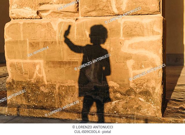 Shadow of woman taking selfie on stone wall