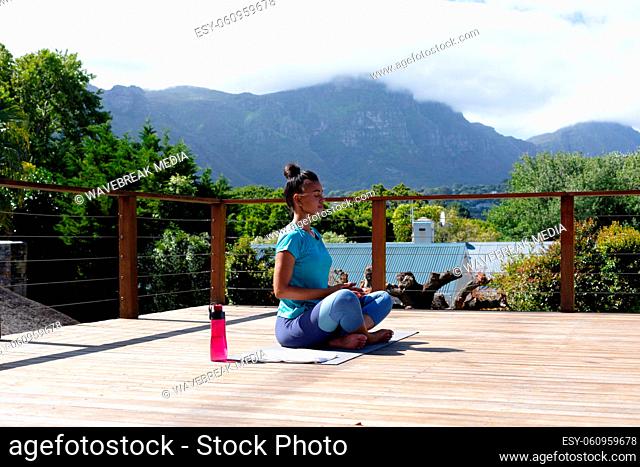 Young african american woman meditating on yoga mat at terrace on sunny day