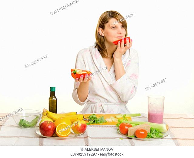 Young beautiful girl in a bathrobe prepares vegetarian salad from vegetables and greens isolated on white background