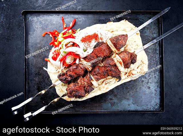 Traditional Greek souvlaki lamb barbecue skewer with paprika, onion and tzatziki offered as top view on a rustic metal tray