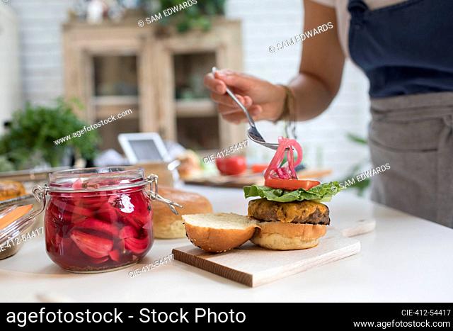 Woman placing pickled onions over cheeseburger in kitchen