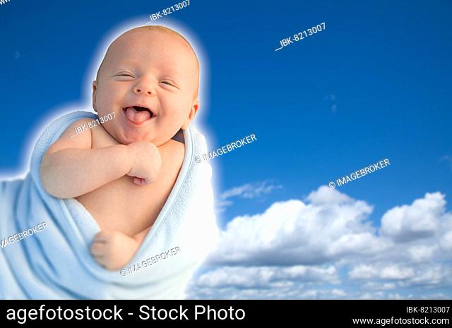 Beautiful laughing baby boy wrapped in his blanket with A blue sky background