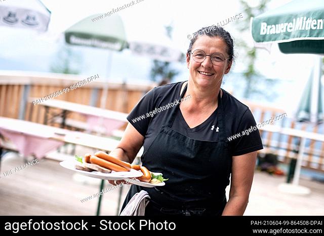 03 June 2021, Bavaria, Mittenwald: Jeannette Lorenz, leaseholder of the Mittenwald Hut, carries two plates of Vienna sausages to a table of guests on the hut's...