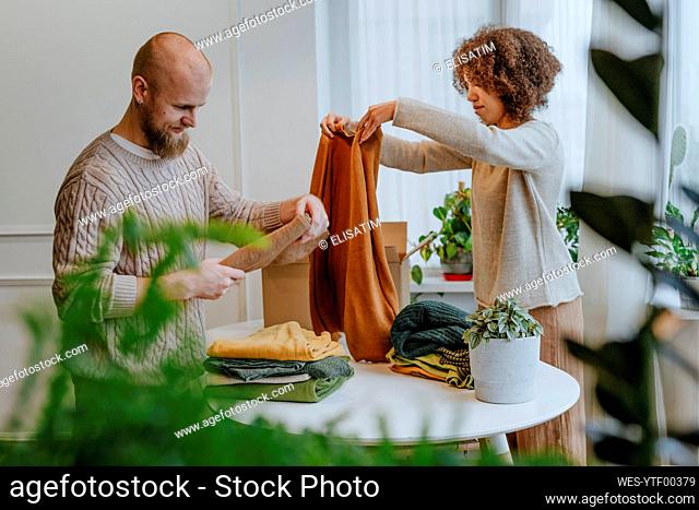 Fashion designer with colleague folding clothes on table