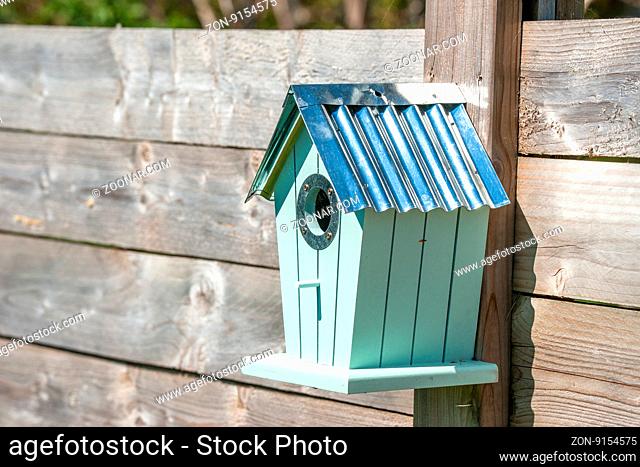 Cute birdhouse hanging on a wooden fence in a garden