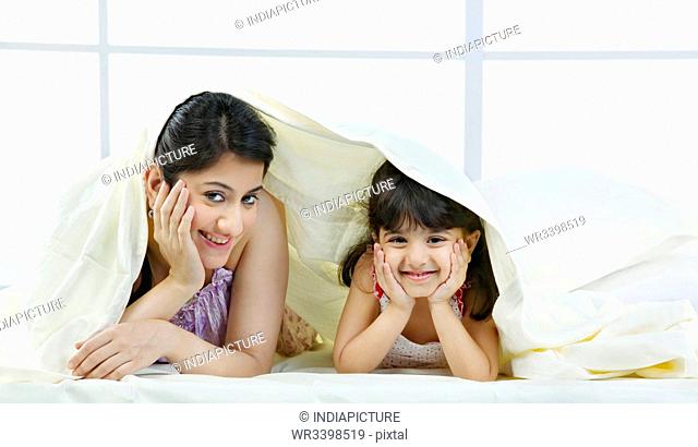 Portrait of mother and daughter under a bed sheet