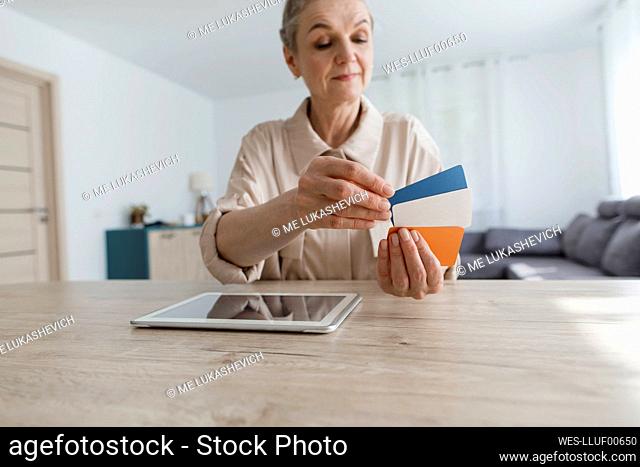 Woman sitting at table at home holding card and using digital tablet