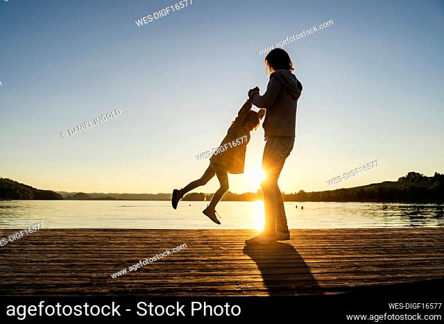 Mother spinning daughter over pier during sunset