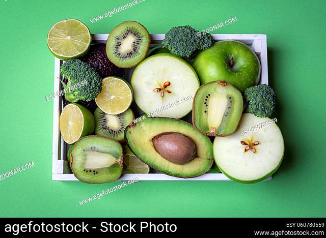 Green kitchen table above view with many fresh fruits and vegetables in a wooden tray. Directly above view with copy space