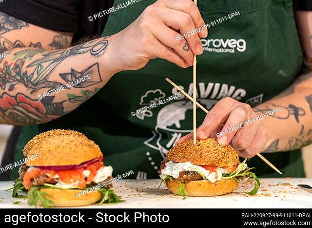 PRODUCTION - 27 July 2022, Bavaria, Nuremberg: A cook prepares burgers with onions, meat tomatoes, remoulade and breaded fish sticks without fish