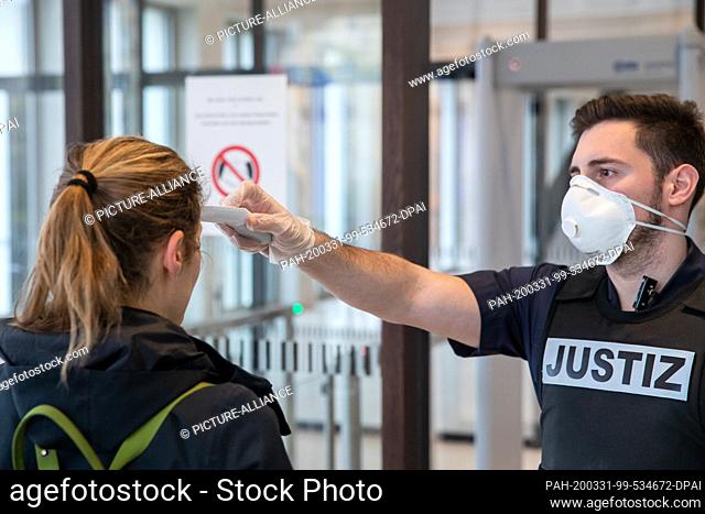 31 March 2020, Bavaria, Nuremberg: A member of the judiciary at the Nuremberg-Fürth Regional Court measures the temperature of a visitor with a clinical...