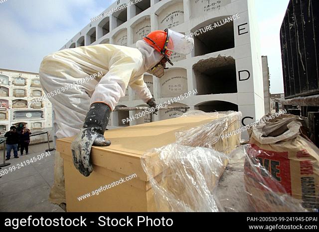 29 May 2020, Peru, Lima: A cemetery worker in a protective suit pushes the coffin of a Covid 19 victim into a niche during a burial at the cemetery ""El Angel""