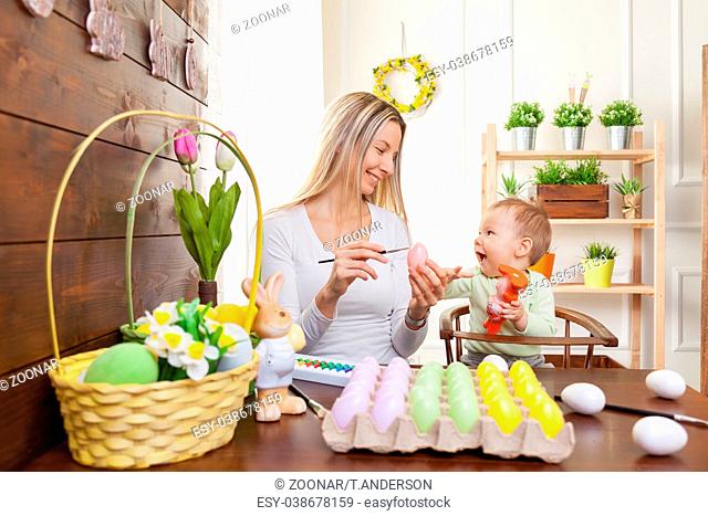 Easter concept. Happy mother and her cute child getting ready for Easter by painting the eggs