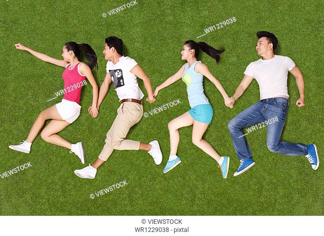 Young people lying on grass hand in hand