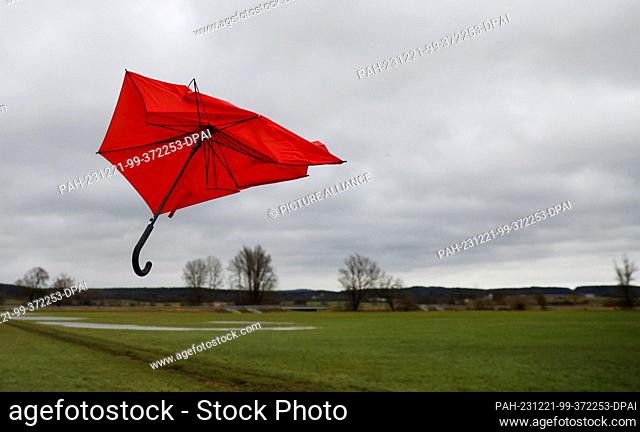 21 December 2023, Baden-Württemberg, Unlingen: A broken umbrella flies in the wind of storm ""Zoltan"" over a meadow where the remains of flood water can still...