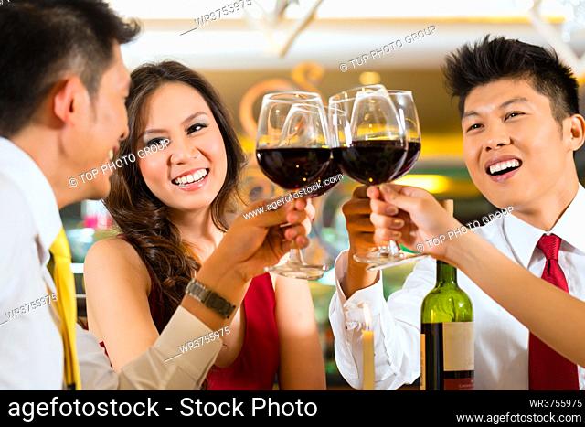 Two Asian Chinese Couples or friends or business people toasting during dinner or lunch in a elegant restaurant with red wine glasses