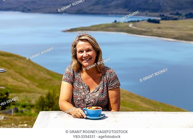 A Middle Aged Woman Sitting With A Cup Of Coffee Overlooking Lake Tekapo, Mt John Observatory Viewpoint, Mackenzie District, South Island, New Zealand