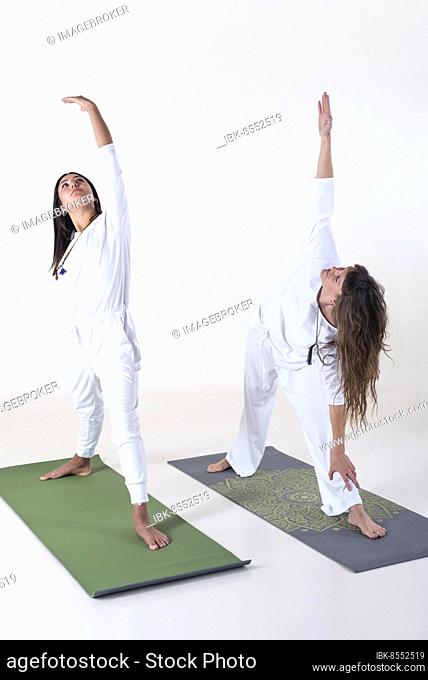 Two women dressed in white doing yoga over white background. Utthita trikonasana yoga pose. Studio shot