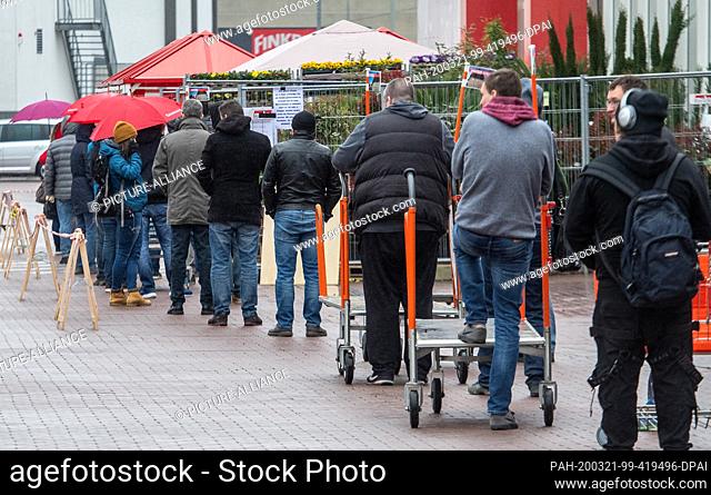 21 March 2020, Baden-Wuerttemberg, Ulm: People stand in a queue in front of a hardware store. Due to the restrictions on the opening hours in neighbouring...