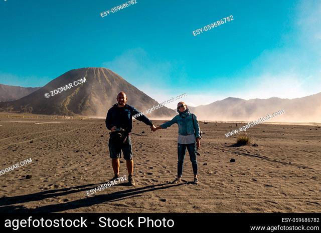 Happy couple travelers standing in a volcanic dusty desert near beautiful Mount Bromo in East Java, Indonesia